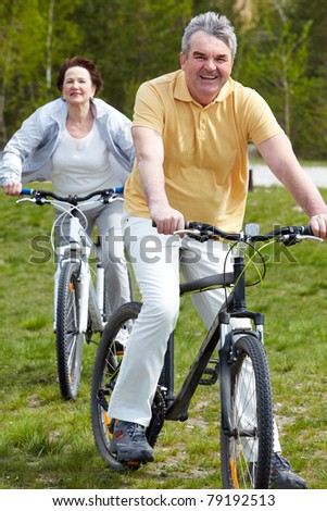 Portrait of happy mature man on bicycle with senior woman on background