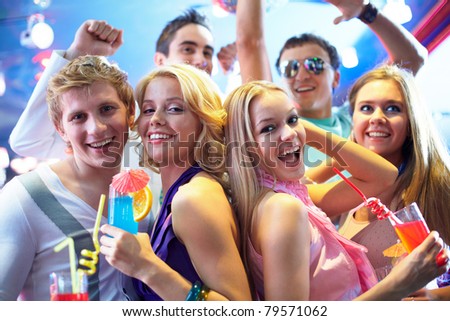 Portrait of cheerful girls with cocktails at party with happy friends near by