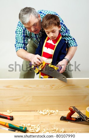 A grandfather teaching a boy to work with saw