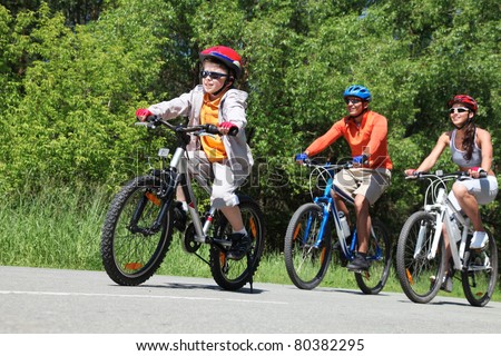 Portrait of happy boy riding bicycle in the park with his parents behind