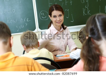 Portrait of smart teacher at workplace looking at schoolkids in classroom