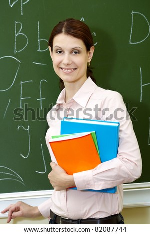 Portrait of smart teacher with books by the blackboard looking at camera