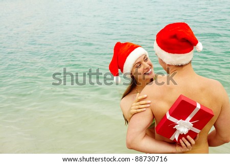 Portrait of happy female in Santa cap embracing her husband while he hiding gift behind his back