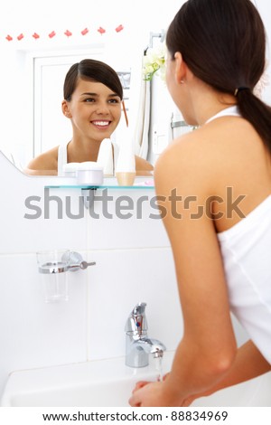 Image of pretty female looking in mirror while washing her hands in the morning
