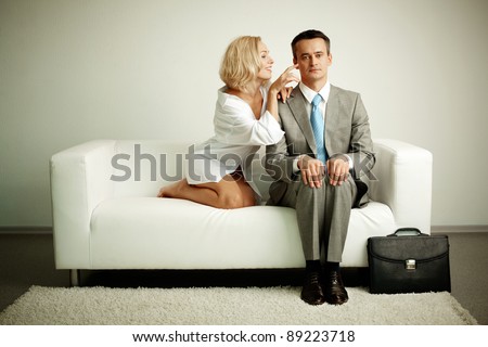 Photo of serious man sitting on sofa with seductive woman teasing him