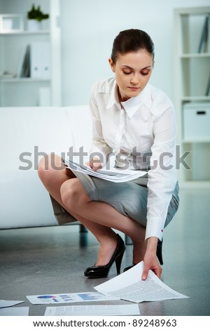 Portrait of serious businesswoman taking papers from the floor in office