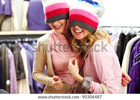 Portrait of two joyful girls with knitted caps on heads laughing in clothing department