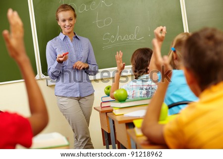 Portrait of smart teacher by blackboard looking at schoolkids in classroom