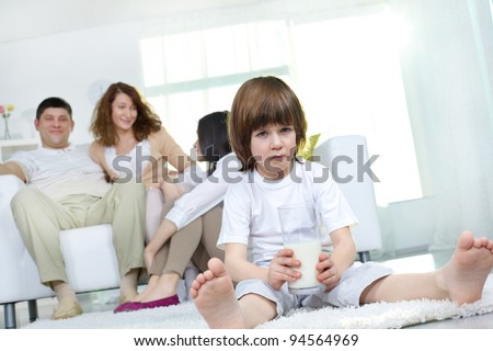 Little boy not wanting to drink milk while the rest of the family having good time together in the background