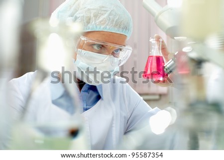 Female scientist looking closely at a beaker with pink fluid