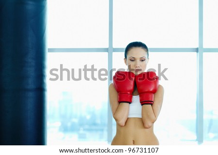 Portrait of sad young woman in red boxing gloves in gym