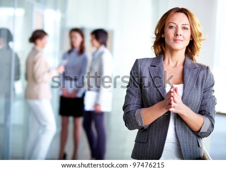 Image of pretty business leader looking at camera with interacting partners at background