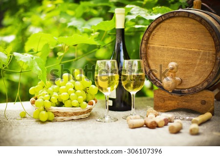 White wine, grapes and oak barrels on background of green leaves