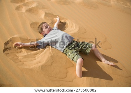 Young boy makes sand angel in on a desert dune