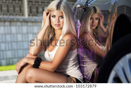 Beautiful young sexy woman near car outdoor. Rich hot blond slim girl with long healthy hair posing with luxury expensive automobile. Fashion model spring-summer
