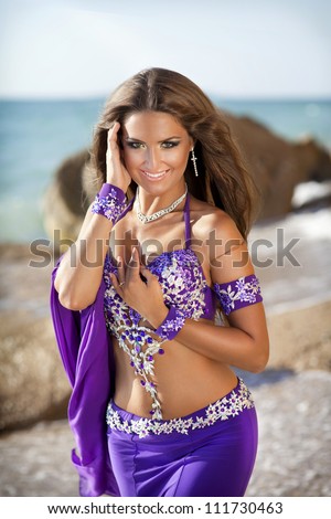 woman belly dancer on sea beach. dancing beautiful slim girl. sexy arabian turkish oriental professional artist in carnival violet costume and diamond jewelry outdoor. exotic bellydance star. Series