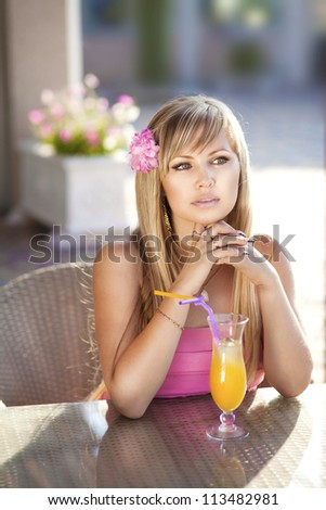 beautiful young woman in cafe with fresh orange juice. Stylish sexy woman waiting for someone at restaurant. Happy rich slim blonde girl with long glossy hair in pink dress resting at bar and posing.