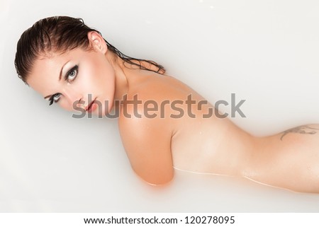 Sexy woman in bath relaxing. Young girl bathing and lying in milk. Alluring brunette posing at bath filled with milk and honey. Model with bright makeup in water. Spa treatments for skin rejuvenation