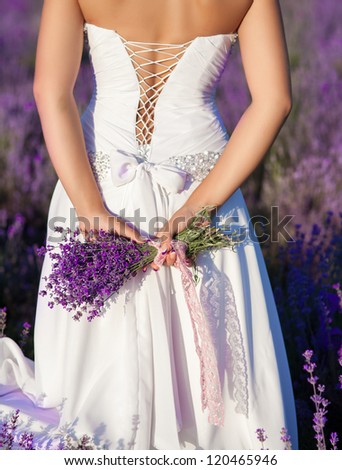 beautiful bride in luxurious wedding dress in purple lavender flowers. Fashion romantic stylish woman with violet bouquet. Alluring slim girl in sunset over lavenda waiting for groom - Provence France