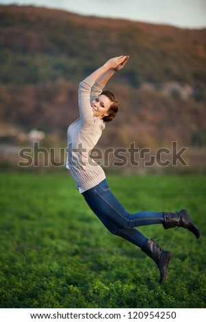 Happy woman Enjoying the nature. Young beautiful girl jumping on fresh air in green field. Provence smiling lady having fun outdoors at sunset