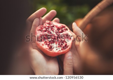 pomegranate in hands of couple in love at sunset outdoors. cutout pomegranate fruit in woman\'s and man\'s hands at sunset lights on autumn nature. fruit on human  hands. romantic and friendship concept