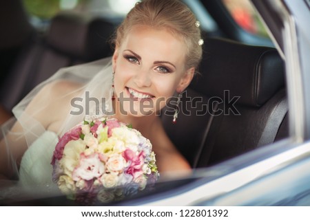 wedding: happy beautiful bride in car with bridal bouquet hairstyle and bright makeup. Blond woman in white dress at wedding day waiting for groom and posing. Concept of happiness and love. Newlywed
