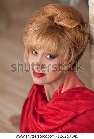 elegant middle aged woman with bright makeup and fashion hairstyle in red scarf posing at home. Rich happy blond stylish businesswoman relaxing and smiling in evening. cheerful middle aged woman