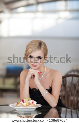Alluring sexy blonde woman in restaurant cafe with ice cream tiramisu cake beautiful girl in black dress hairstyle and makeup eating dessert. Beauty fashion slim model rich retro lady in vintage dress