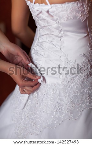 Morning bride. maid of honor helping the bride with her dress. bridesmaid tying bow on wedding dress. helping to lace up bride\'s wedding dress