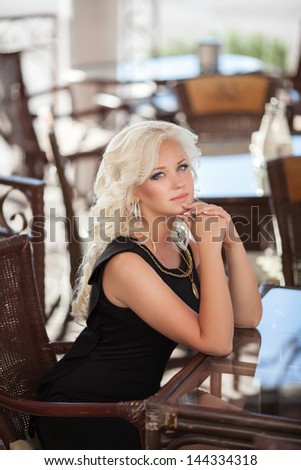 Beautiful happy woman in cafe restaurant sexy blonde girl in black dress on dating with retro curly hairstyle and makeup. Glamour woman  smiling in fashion trendy dress outdoors. Woman resting at cafe