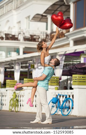 Teenage couple embracing on dating with bunch of balloons hearts. Beautiful Young Couple man and woman in love. Smiling man and woman hugging. happy loving couple. Young couple in love outdoor.