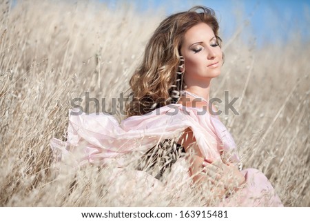 Beautiful sexy woman walking outdoors, young healthy woman in summer field. perfect skin, long curly hair, bright makeup, sexy body. girl in morning in wheat meadow