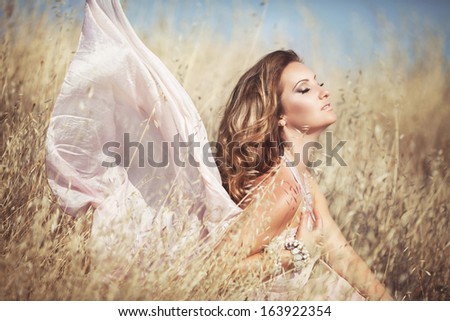 Healthy beautiful woman walking outdoors. Alluring young woman in wheat field,  delicate sensual woman on nature. perfect skin, curly hair.
