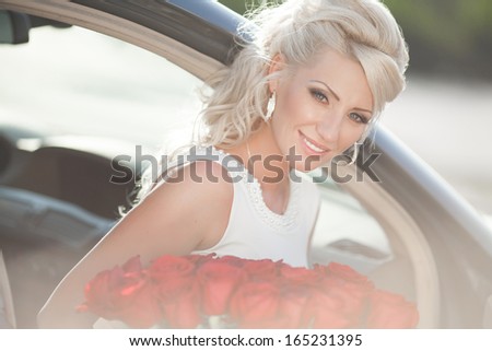 Happy woman in luxury car with roses flowers at Valentine\'s day. Sexy woman with bouquet in car. Beautiful rich woman smiling portrait. Sensual young girl with car. soft light shot.