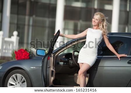 Happy woman in luxury car with roses flowers at Valentine's day. Sexy woman with bouquet in car. Beautiful rich woman smiling portrait. Sensual young girl with car. soft light shot.