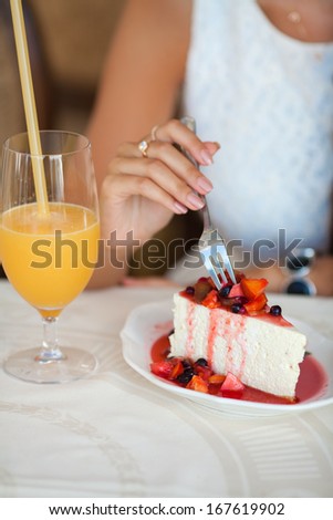 Woman eating berry cheese cake and drinking juice at cafe.  young woman sitting in cafe eating cake. Breakfast in restaurant.