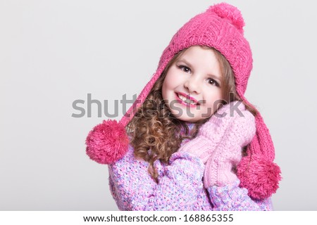 Happy child in winter hat and gloves in woolen sweater. Cute little girl in winter clothes and woolen accessories. Happy kid winter fashion. Studio, isolated, white background.
