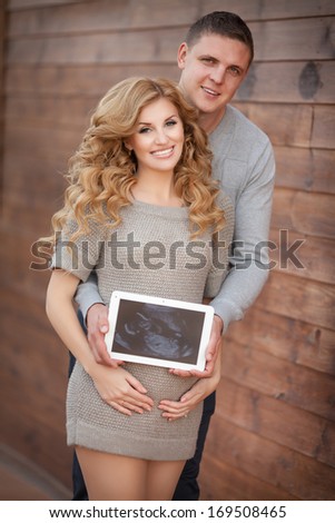 Pregnant woman with husband holding ultrasound scan on her tummy, healthy pregnancy. Happy pregnant couple outdoors. Pgegnant family. Concept.