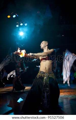 The young sexual fakir man fire eater actor   eating fire dangerous fiery fascinating performance in circus at night  and breathing fire and beauty arabic bellydancers with shawl