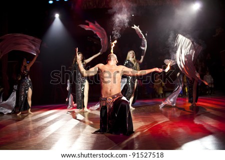The young sexual fakir man fire eater actor   eating fire dangerous fiery fascinating performance in circus at night  and breathing fire blowing fire from his mouth and wonderful arabic bellydancers