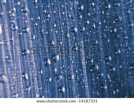 Water drops on a metal surface. The metal structure at light consists of points of different colors. Macro.