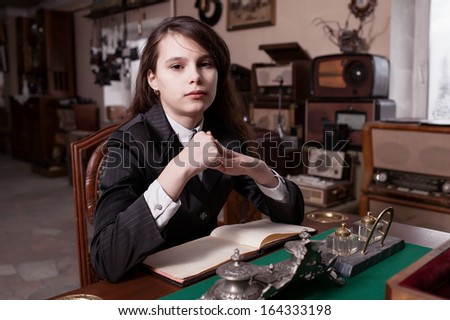 Fashionable girl in pin striped suit sat on wooden chair in antique shop.
