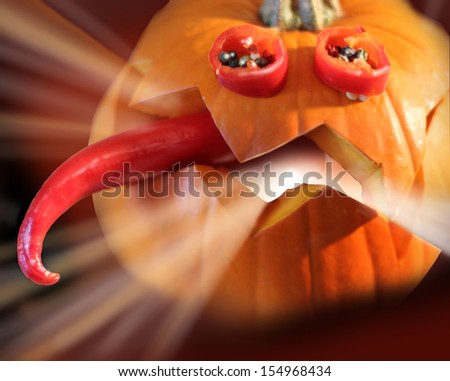 Halloween decoration of a pumpkin. Funny pumpkin for the Halloween holiday table decoration. Glowing inside, with the tongue of hot pepper and eyes on a dark background
