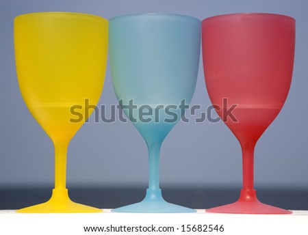 Three plastic goblets sitting on a white deck railing that are also the three primary colors in art.