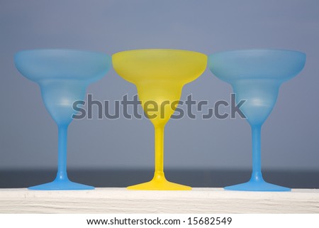 Three plastic goblets sitting on a white deck railing in the sun.