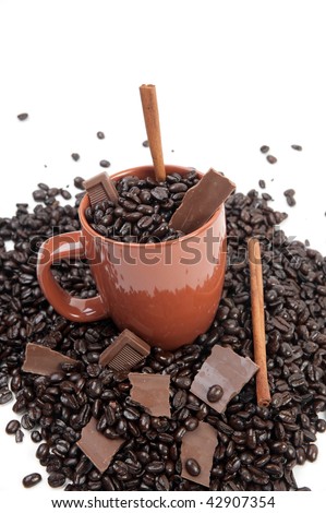 Coffee mug full of coffee beans on pile of coffee beans with chocolate and cinnamon sticks