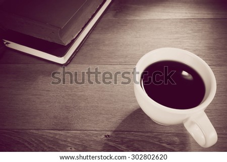 cup of black coffee and book on wooden table, style vintage.