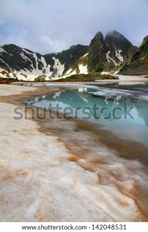 Glacier lake with ice and snow melting in foggy weather on the mountain