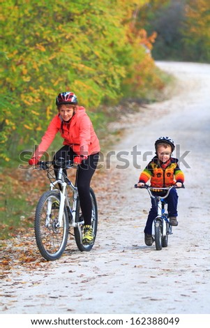Small child accompanied by his mother during bike ride in autumn forrest