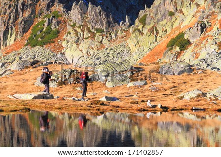 Hikers and mountains reflected by calm waters of glacier lake